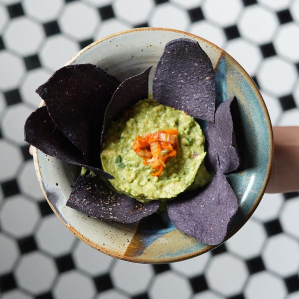 Overhead view of guacamole topped with kimchi, surrounded by blue corn chips in a rustic bowl.