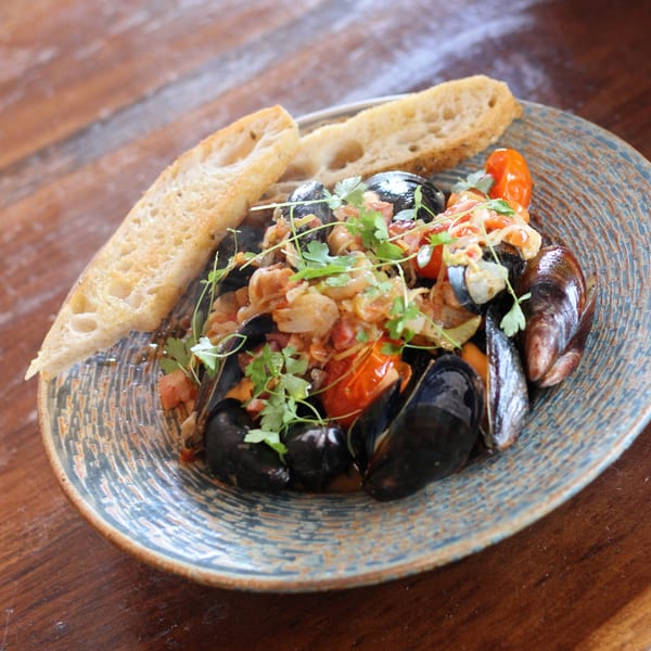 Steaming mussels in a rich tomato and onion sauce, garnished with fresh herbs and served with crusty bread.