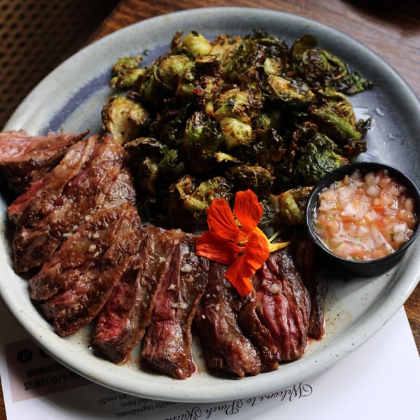 Pinch Kitchen+Bar's sliced steak with roasted Brussels sprouts, salsa, and an orange flower garnish.