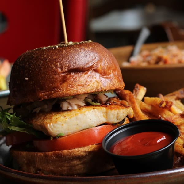 A grilled fish sandwich with lettuce, tomato, and fries with ketchup on a dark plate.